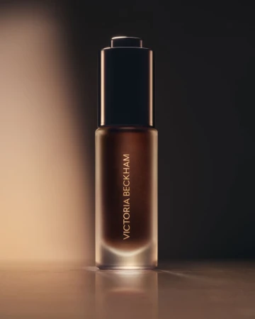 Victoria Beckham Beauty foundation bottle in a beauty shot featuring a sleek bottle design with a dropper, against a soft gradient background.