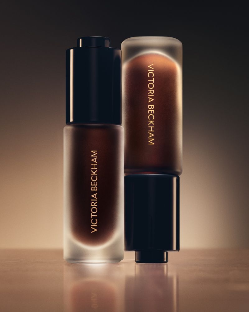 Two Victoria Beckham beauty bottles are staged in a close-up, highlighting the brand's makeup and skincare line with luxury packaging.