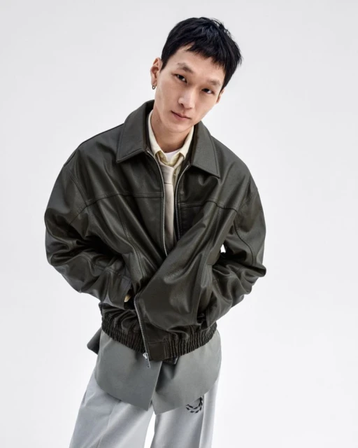 Portrait of an Asian adult male wearing a leather jacket and grey pants, posing in a photo studio setting, against a clean white backdrop.