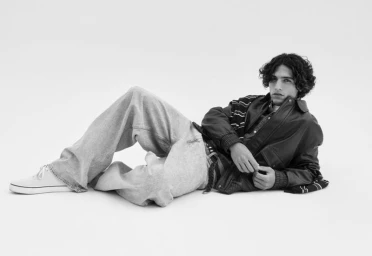 Model in a leather jacket and wide-leg jeans lying on a white seamless studio backdrop in a black-and-white photograph