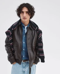 Model in brown leather jacket over a blue denim shirt against a white seamless background