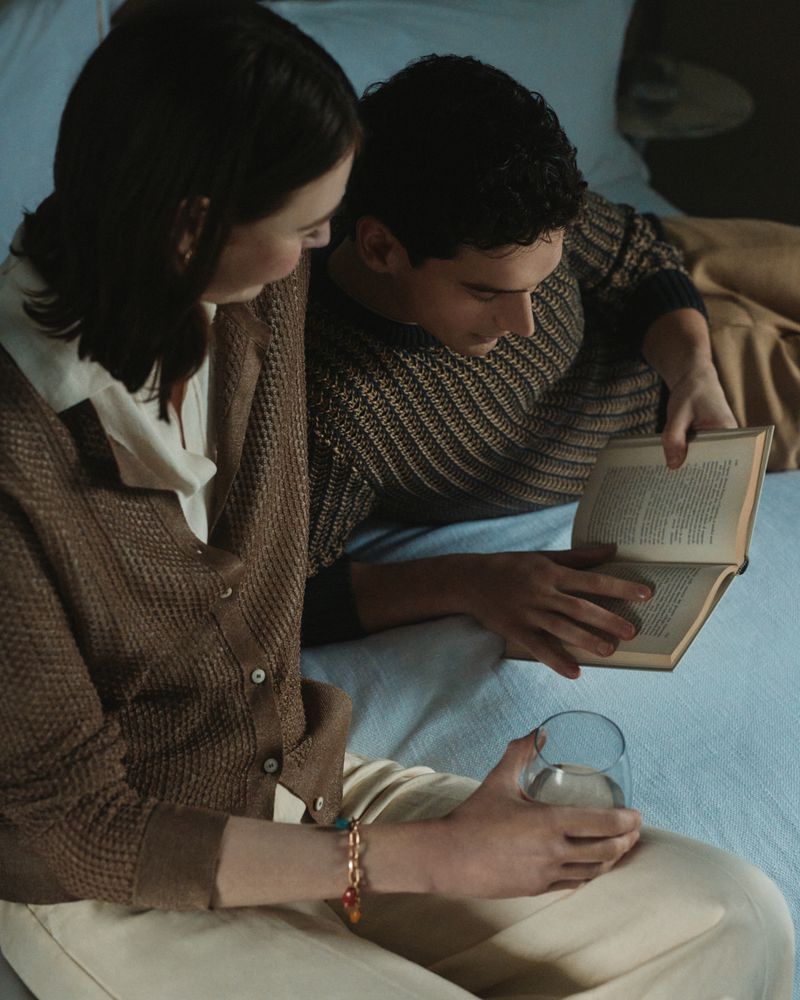 Young couple reading a book together on a bed with soft lighting.  The man holds the book while the woman looks on attentively.