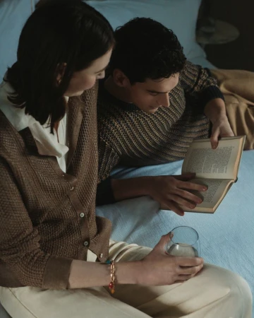 Young couple reading a book together on a bed with soft lighting.  The man holds the book while the woman looks on attentively.
