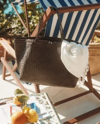 Dark brown woven leather tote bag hanging on a blue and white striped deck chair with a white towel