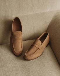 A pair of tan suede penny loafers resting on a textured fabric upholstered sofa surface.