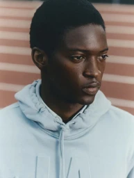 Portrait of a black man wearing a light blue hoodie against a blurred stadium track background for Sfera.