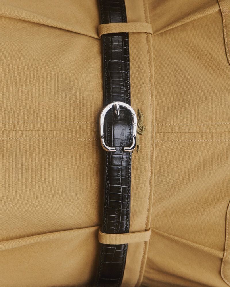 A close-up shot focuses on a black textured belt with a silver buckle, secured on a tan fabric garment featuring vertical stitching details.