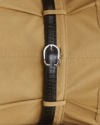 Close-up of a black embossed leather belt with a silver buckle worn over a beige garment for Longchamp.