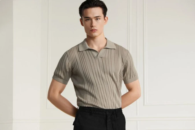 Model wearing a grey knitted polo shirt against a pale paneled architectural interior wall