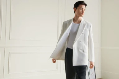 Model in white double-breasted blazer and dark trousers standing against white wall paneling