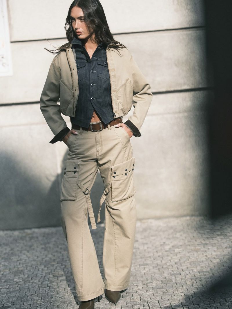Model standing outdoors wearing khaki cargo pants, a matching cropped jacket, and a dark denim button-down shirt.