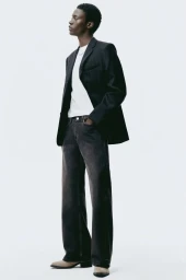 Full-length portrait of a male model wearing a dark blazer, white t-shirt, and dark jeans against a white seamless background