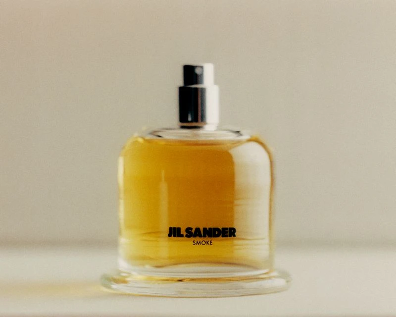 Close-up studio shot of a clear glass perfume bottle with amber-colored liquid and a black label, set against a neutral background.