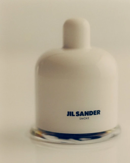 Studio shot of a white ceramic perfume bottle with a clear glass base, featuring the Jil Sander brand and 'Smoke' fragrance name.