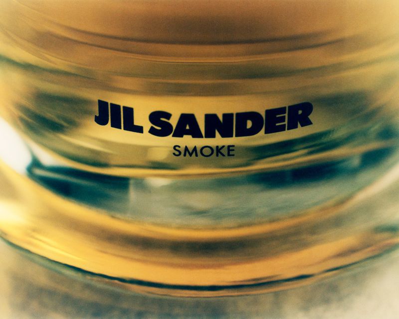 Extreme close-up shot of a Jil Sander Smoke fragrance bottle with amber glass and bold black typography.