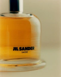 Close-up product shot of a Jil Sander Smoke fragrance bottle filled with amber liquid against a neutral background.