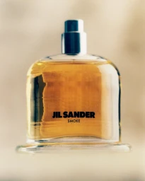 Jil Sander Smoke fragrance bottle filled with golden liquid against a warm neutral background