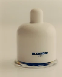 A white Jil Sander Smoke fragrance bottle sitting on a light surface against a minimalist neutral backdrop.