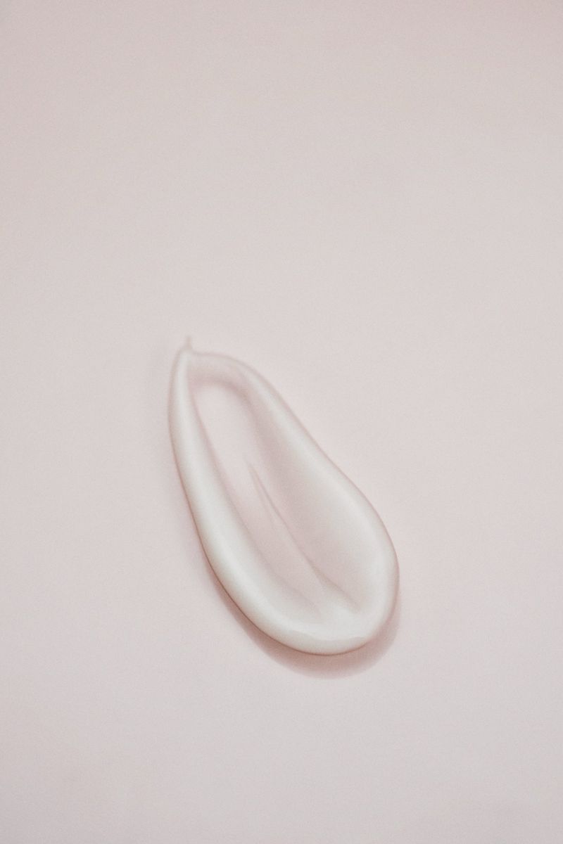 Close-up studio shot of a smear of white cream on a soft pink background, highlighting texture and skincare product.
