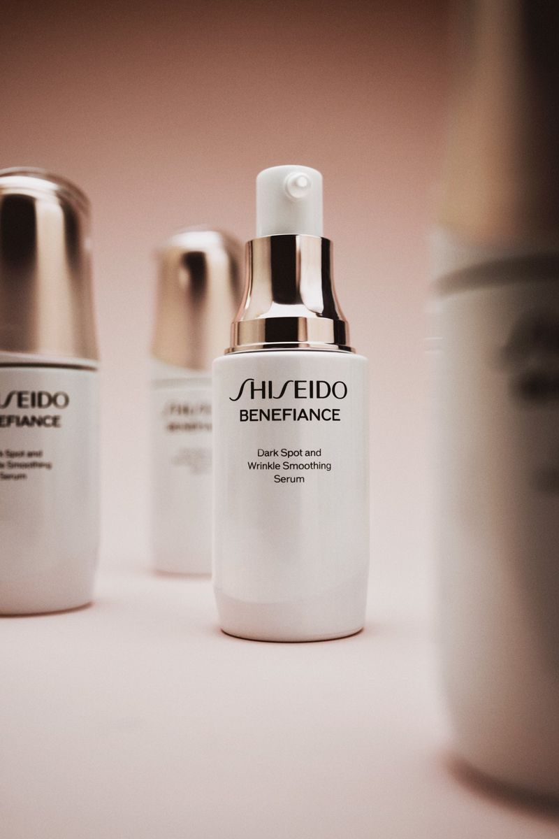 Close-up of white Shiseido Benefiance serum bottles with gold accents against a soft pink background, skincare product photography.