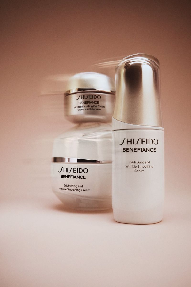 Shiseido Benefiance skincare products in white and silver packaging, featuring wrinkle smoothing cream and dark spot serum against pink background.