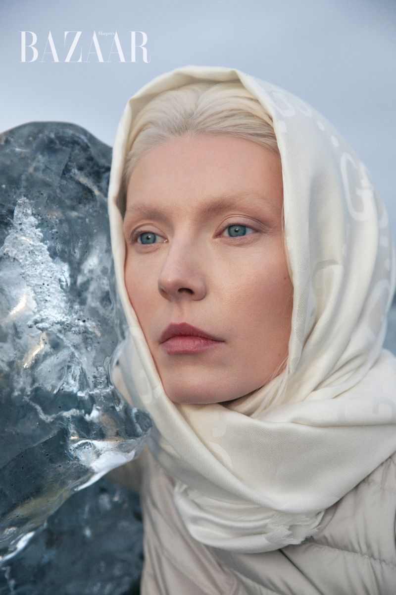 Close-up of a fair-skinned woman in a hooded headscarf alongside a glacier fragment, against a pale blue sky, shot for Bazaar.