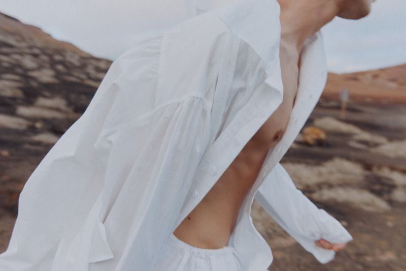 An adult in white clothing stands outdoors in a desert landscape, creating a visually striking and minimalist composition.