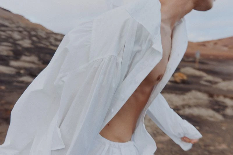An adult in white clothing stands outdoors in a desert landscape, creating a visually striking and minimalist composition.