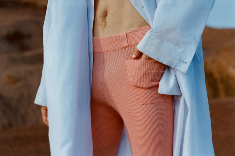 Close-up of person wearing pink pants with hand in pocket and light blue jacket against an outdoor background. Fashion editorial shot.