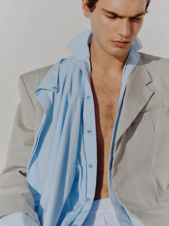 Close-up portrait of a male model wearing an unbuttoned blue shirt and a grey jacket against a white background