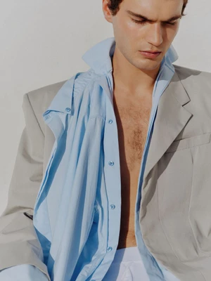 Close-up portrait of a male model wearing an unbuttoned blue shirt and a grey jacket against a white background