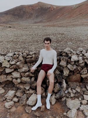 Model Lars Jammaers sits against a dry stone wall in an arid mountainous landscape for The Greatest Magazine Issue 29