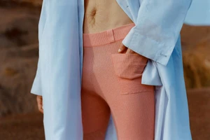 Close-up of a person wearing ribbed pink trousers and an open white coat outdoors against a natural rocky background