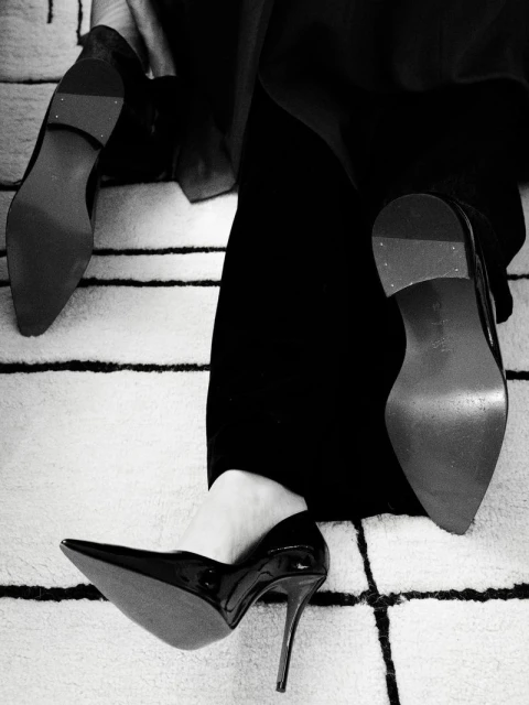 Close-up of woman in black pants and shiny black high heels, with a cream and black geometric rug visible underneath.