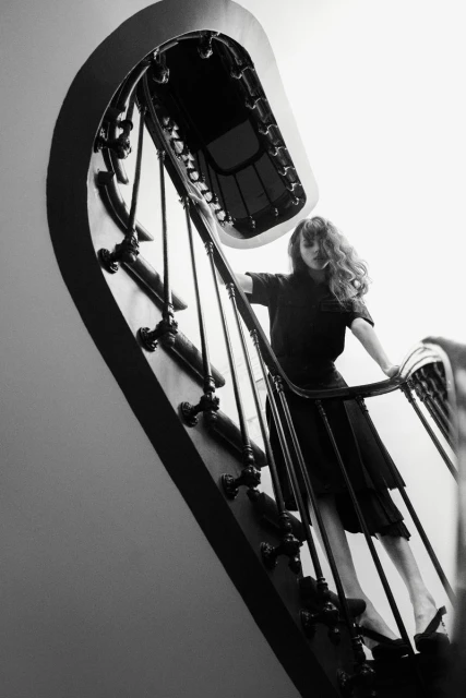 Monochrome portrait of a woman in a dark dress on a decorative staircase, captured from a low angle, emphasizing architectural details.
