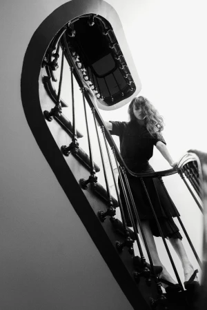 Monochrome portrait of a woman in a dark dress on a decorative staircase, captured from a low angle, emphasizing architectural details.