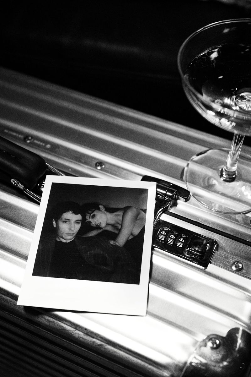 Black and white image of a photograph of two people next to a cocktail glass on a metal surface with combination lock.
