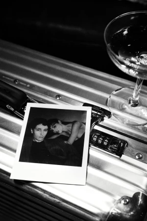 Black and white image of a photograph of two people next to a cocktail glass on a metal surface with combination lock.