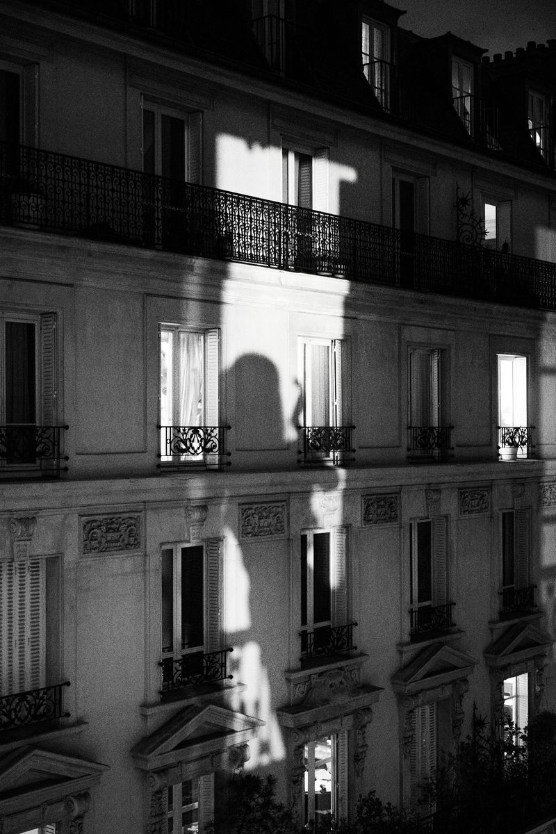 Black and white architectural photo of an apartment building at night with illuminated windows and a silhouette of a person in one window.