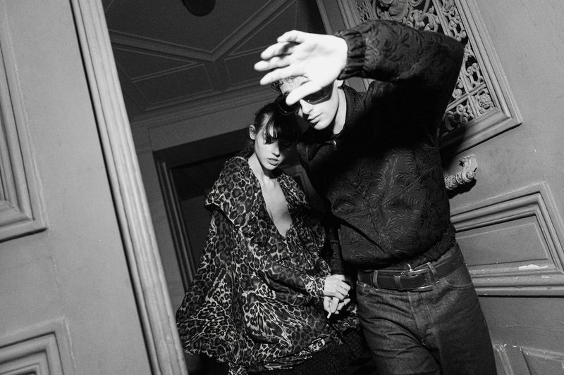 Black and white fashion shot of a stylish couple walking down stairs; the man shields his face, and the woman wears a leopard print coat.