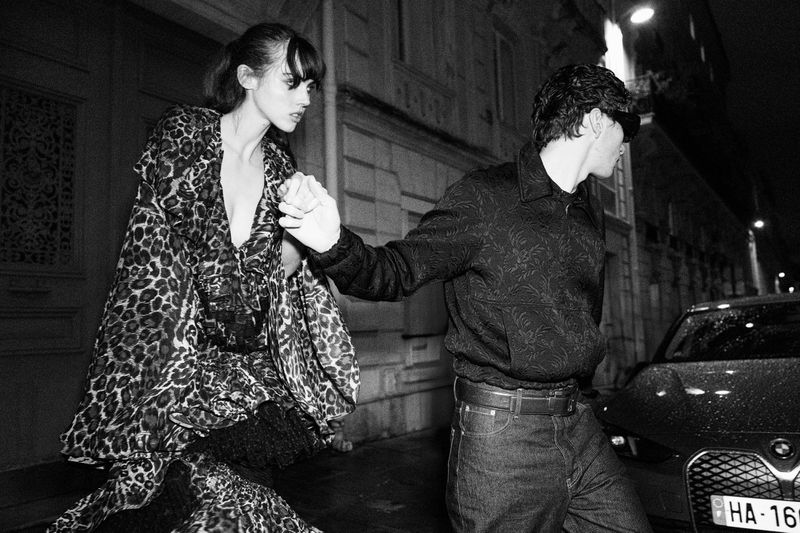 Black and white fashion shot of a female model in a leopard print dress and a man in a dark patterned shirt in an urban environment.