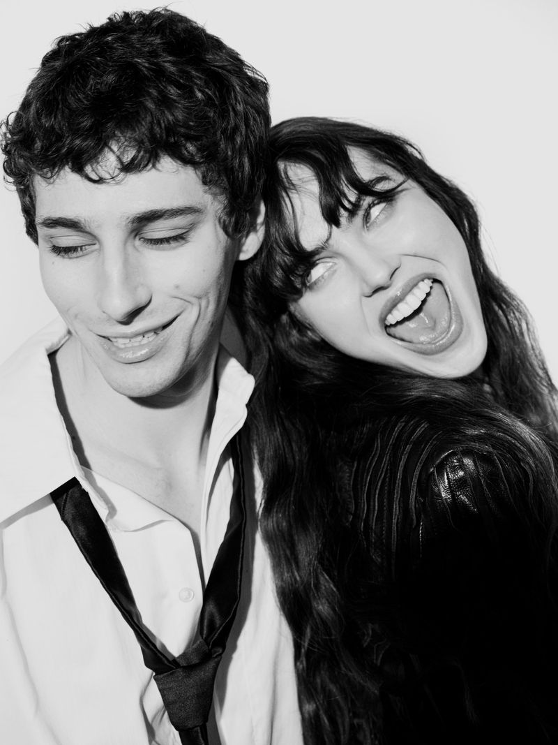 Black and white portrait of a smiling couple, with the woman leaning on the man's head, showcasing their close and playful relationship.