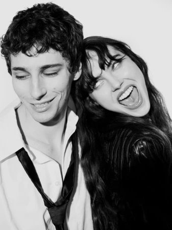 Black and white portrait of a smiling couple, with the woman leaning on the man's head, showcasing their close and playful relationship.