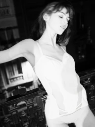 Black and white portrait of a woman leaning against an ornate dark balcony railing in a white camisole