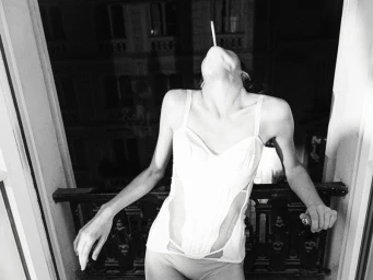 Model in a white corset holding a cigarette outdoors against a dark building exterior at night