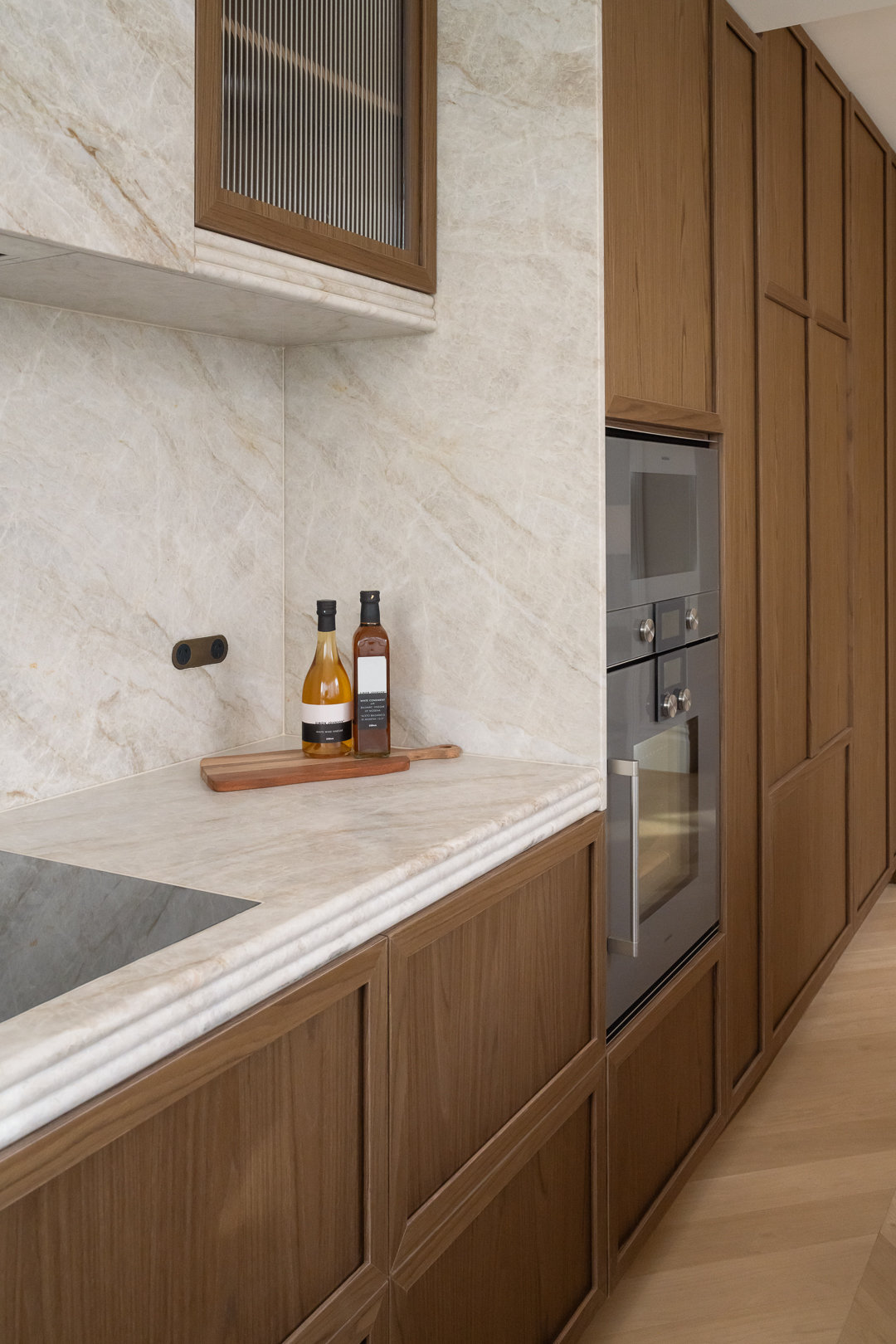 Modern kitchen interior featuring wood cabinetry, stone countertops, stainless steel oven, and decorative oil bottles. Interior design.