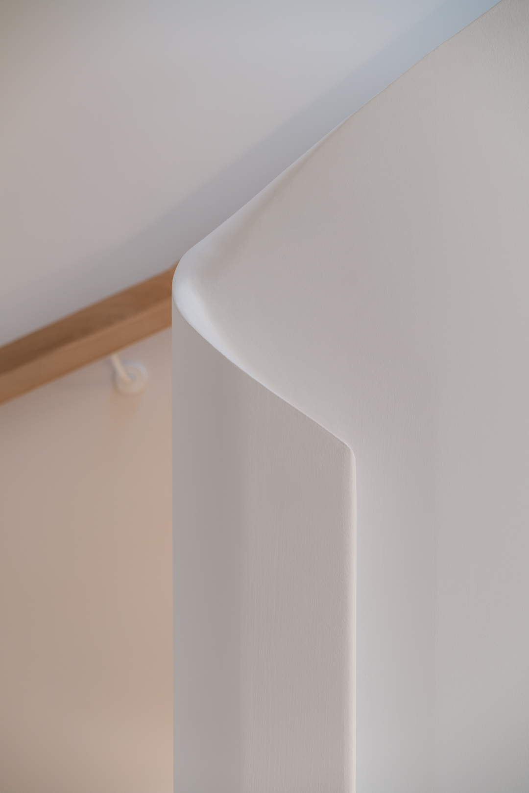 Close-up architectural detail of a curved white wall corner and wooden trim by By Soma Architects.