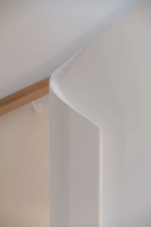 Close-up architectural detail of a curved white wall corner and wooden trim by By Soma Architects.