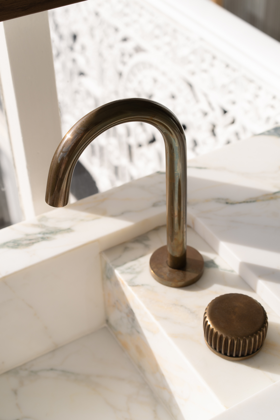 Close-up of a modern bronze faucet and control on a white marble countertop in an indoor bathroom setting. Bright natural light.