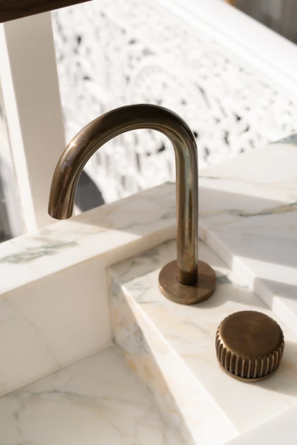 Close-up of a modern bronze faucet and control on a white marble countertop in an indoor bathroom setting. Bright natural light.
